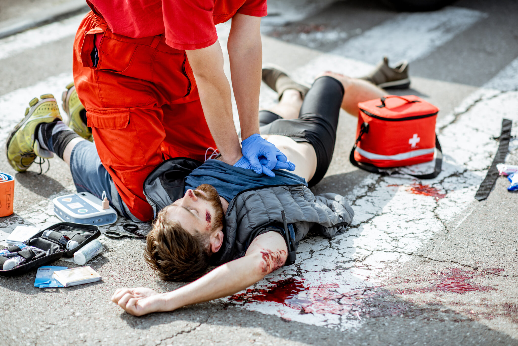 Ambluence worker applying emergency care to the injured bleeding man lying on the pedestrian crossing after the road accident